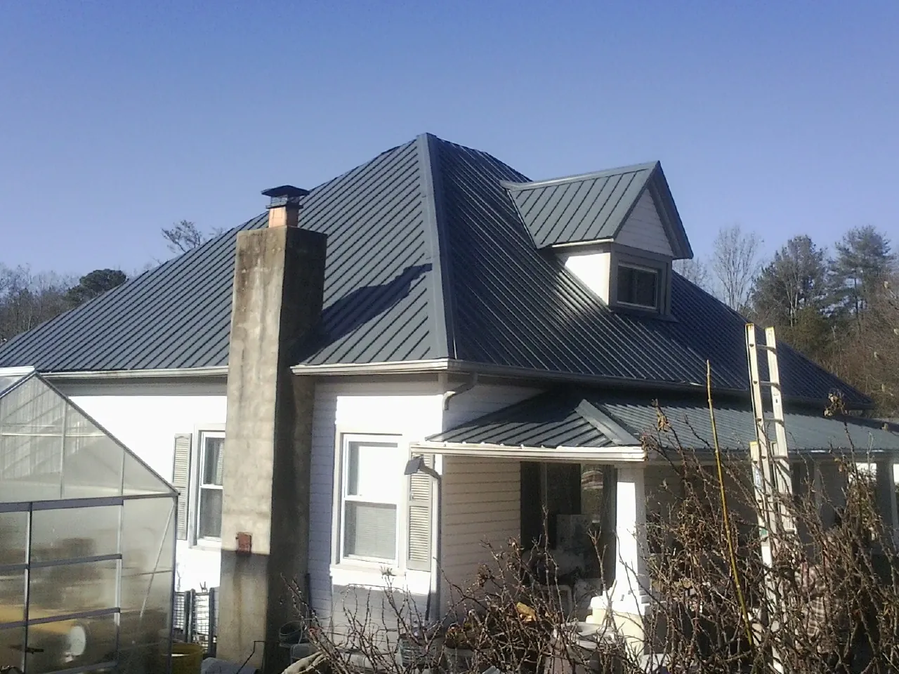 Dark blue standing seam metal roof on a white farmhouse with dormer — Slate & Tile Roof Repair by Roofing Brothers in Jonestown