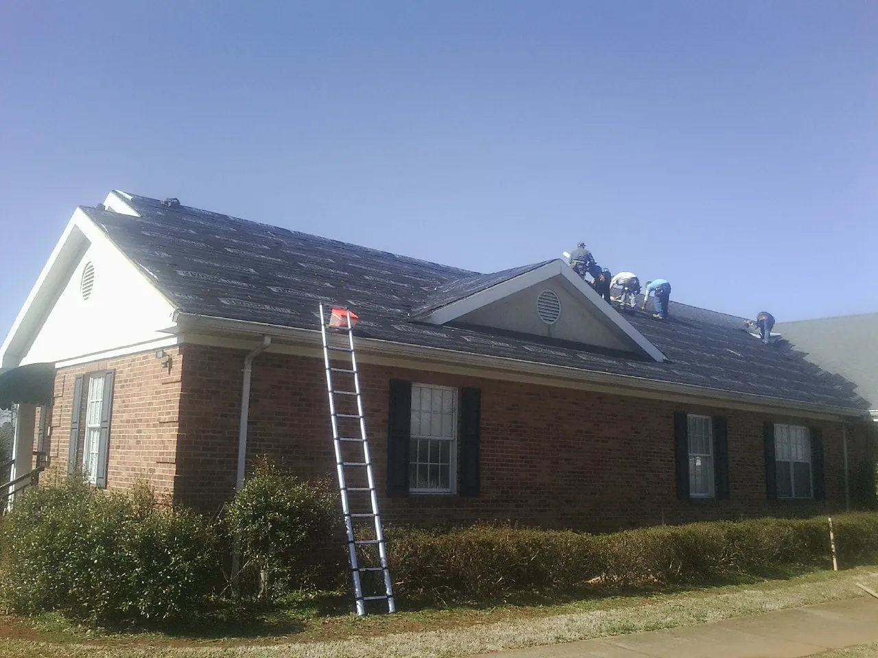 Crew tearing shingles off a brick ranch roof with a ladder set — Emergency Roof Repair work by our crew in Jonestown