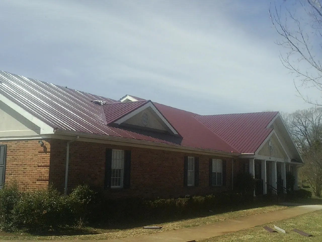 Red metal roof with gabled entries on a long brick building, from a Hail Damage Roof Repair job in Jonestown
