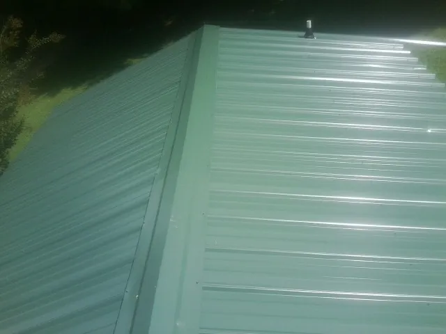 New green metal panels meeting at the ridge of a roof — Flat Roof Repair work by our crew in Jonestown