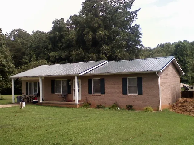 Gray metal roof on a brick ranch house with a side carport in Jonestown