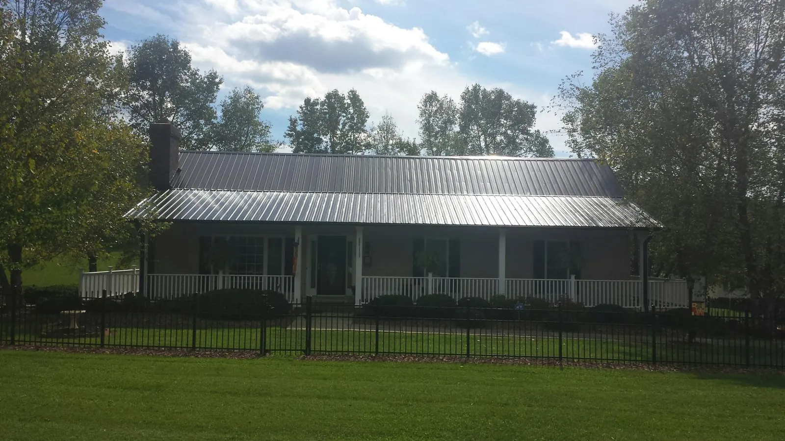Gray metal roof on a brick ranch with a full width front porch — Gutter Guard Installation work by our crew in Jonestown