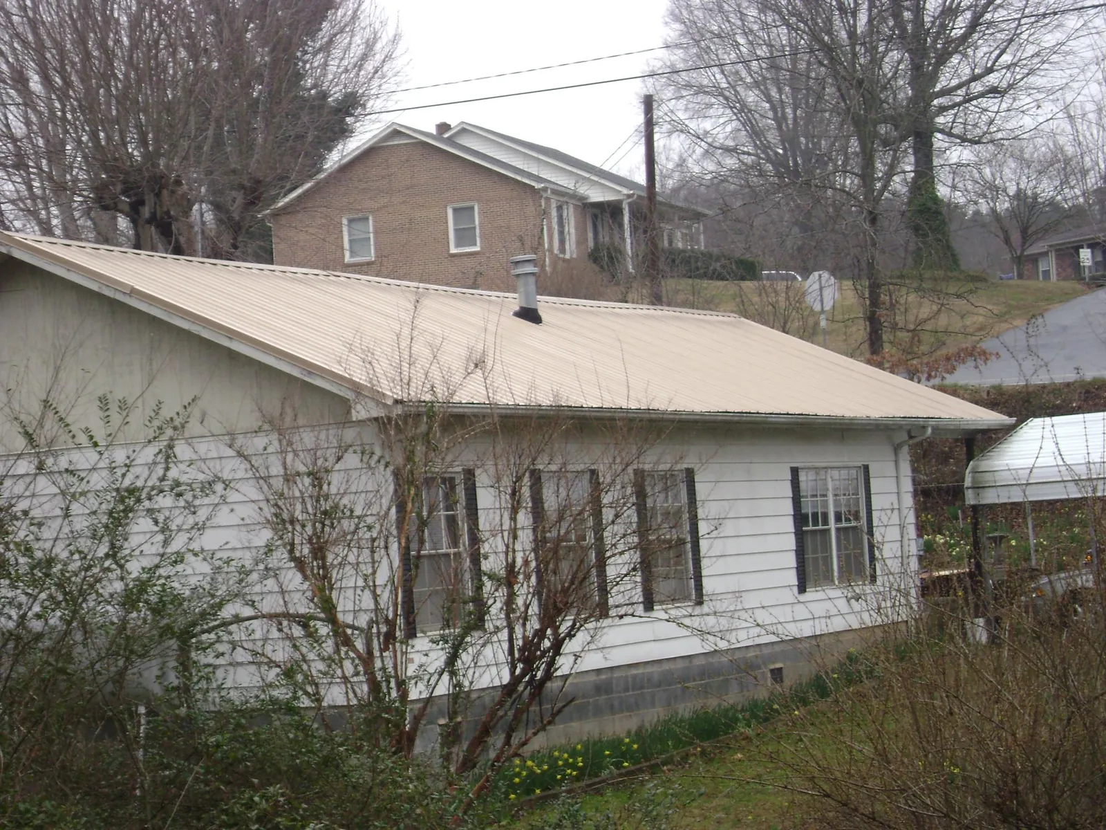 Tan metal roof on a white sided house set into a hillside — Commercial Roofing by Roofing Brothers in Jonestown