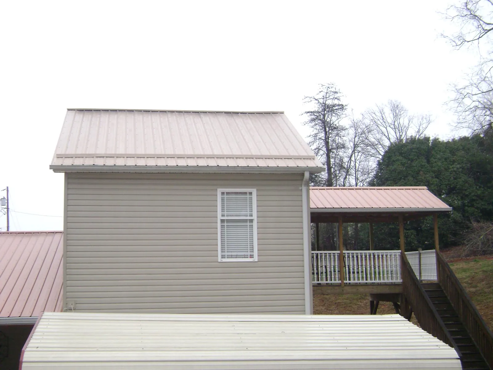 Tan metal roofs on a two story addition and attached porch, from a Roof Replacement job in Jonestown